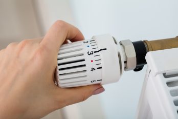 Detailansicht eines Heizungsthermostats, welches von einer Hand gedreht wird