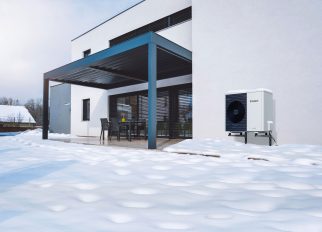 Vor einem Neubau steht eine aroTHERM plus Luft/Wasser-Wärmepumpe im Schnee.