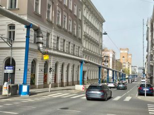 Über einer Hauptstraße zwischen schönen alten Mehrfamilienhäusern verläuft eine Fernwärmeleitung.