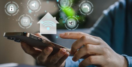 Eine Hand bedient ein Smartphone, in Kreisen ringsherum verschiedene Smart-Home-Symbole