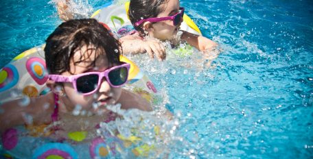 Zwei kleine Mädchen mit Sonnenbrille schwimmen mit Schwimmring im Wasser