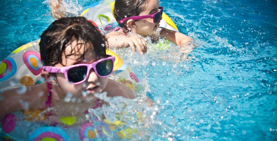 Zwei kleine Mädchen mit Sonnenbrille schwimmen mit Schwimmring im Wasser