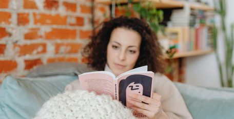 Eine Frau sitzt zugedeckt auf einem Sofa und liest ein Buch