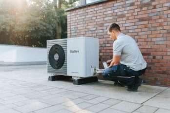 Die Außeneinheit der Wärmepumpe aroTHERM Split plus, rechts daneben ein hockender Fachhandwerker